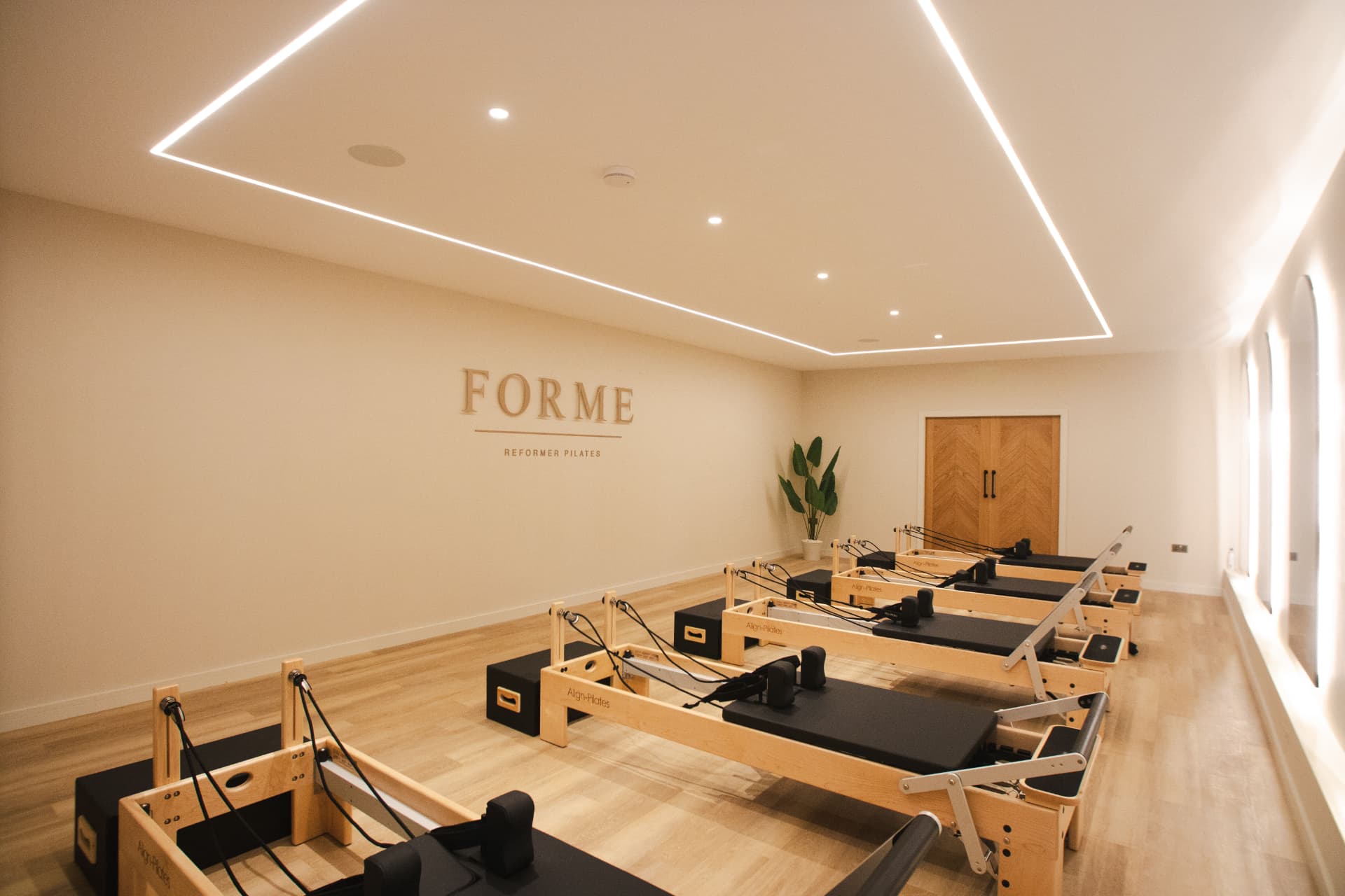 The FORME studio with reformers, warm wall lighting and the FORME Reformer Pilates sign